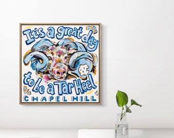 May include: A framed painting featuring a blue and white ram mascot with the text "It's a great day to be a Tar Heel Chapel Hill".
