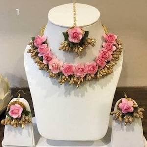 Puede incluir: Un conjunto de joyas de flores rosas con un collar, pendientes y un maang tikka. El conjunto está hecho de flores artificiales y cuentas doradas.