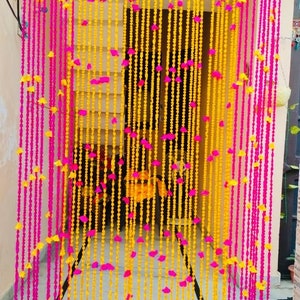 Può includere: Una tenda da porta decorativa realizzata con ghirlande di fiori rosa e gialli. Le ghirlande sono infilate insieme per creare un effetto tenda. La tenda è appesa a una porta.