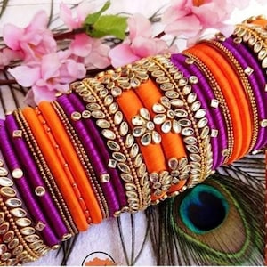 Peut inclure: Un ensemble de bracelets en fil de soie colorés avec des accents dorés et des embellissements décoratifs. Les bracelets sont dans des tons d'orange et de violet.