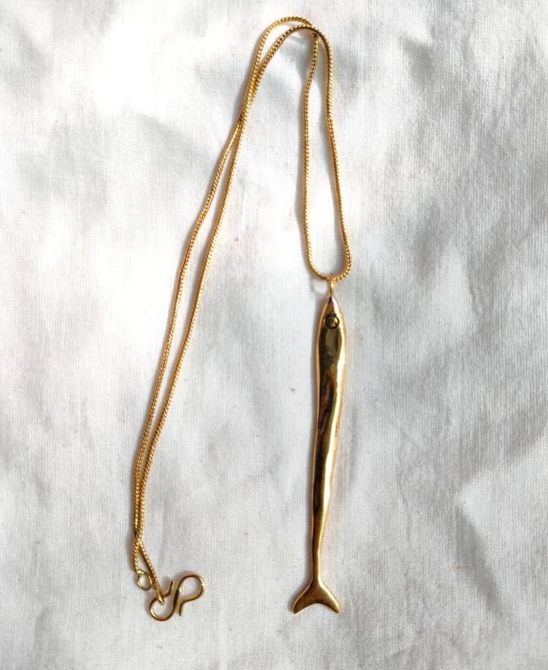 Op de afbeelding: Een gouden ketting met een lange, dunne, gouden vis hanger.