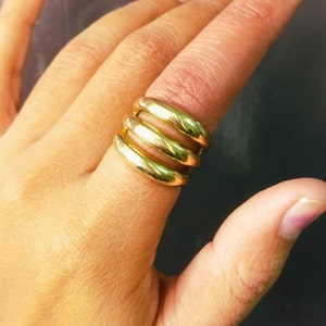 Puede incluir: Un anillo de oro con cuatro bandas apiladas una encima de la otra. El anillo se lleva en un dedo.