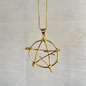 Puede incluir: Un collar de oro con un colgante de estrella de cinco puntas hecho de alambre retorcido.