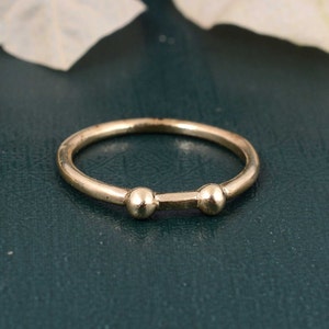 May include: A simple gold ring with two small round beads on the band.
