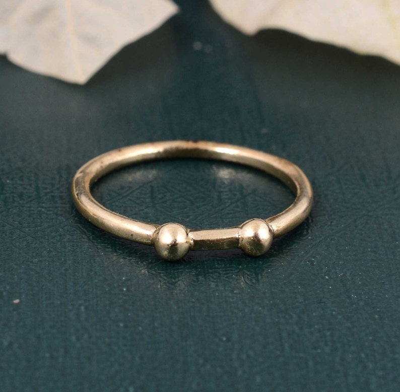 May include: A simple gold ring with two small round beads on the band.