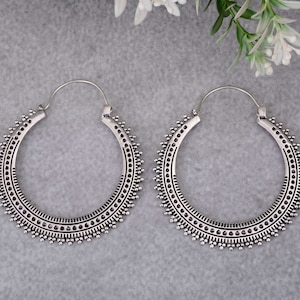 May include: A pair of silver hoop earrings with a detailed, intricate design. The earrings are large and circular, with a textured surface.