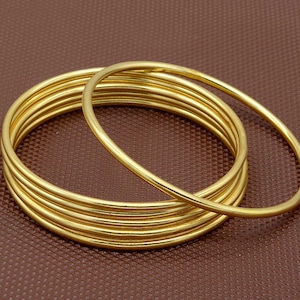 Può includere: Un set di sette braccialetti rigidi dorati impilati uno sull'altro. I braccialetti sono lisci e lucidi.