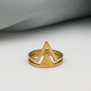 May include: A gold-toned ring with a geometric design featuring two overlapping triangles.