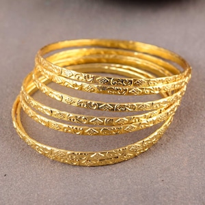 Pode incluir: Um conjunto de sete pulseiras douradas com padrões florais e geométricos intrincados. As pulseiras estão empilhadas umas sobre as outras, criando um visual em camadas.