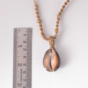 Puede incluir: Un collar con un colgante de concha de cauri marrón, un cordón marrón y cuentas doradas. El collar mide aproximadamente 50 cm de largo.