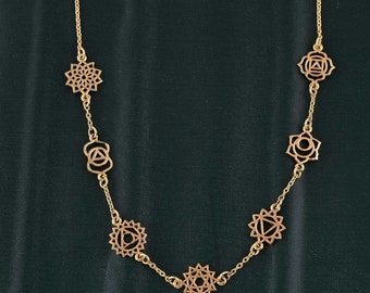 May include: A gold chain necklace with seven charms, each featuring a different chakra symbol. The symbols are intricate and detailed, and the chain is delicate and feminine.