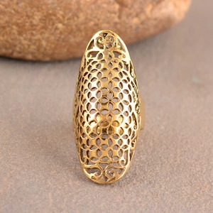 May include: A gold-toned, oval-shaped ring with a delicate, intricate, cutout design. The ring is made of metal and has a smooth, polished finish.
