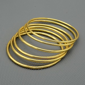 Può includere: Un set di sei braccialetti dorati impilati uno sull'altro. I braccialetti sono lisci e lucidi.