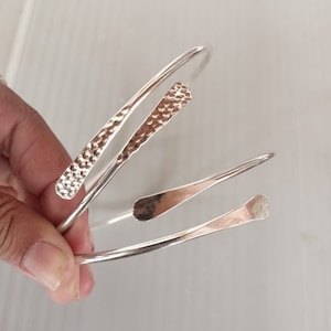 May include: Three silver bracelets with hammered textures. The bracelets are stacked on top of each other.