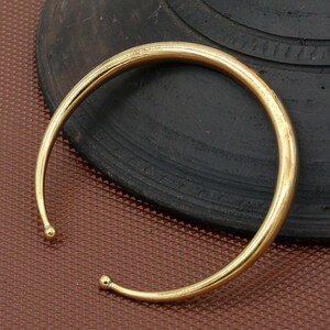 Puede incluir: Un brazalete simple de oro con bordes redondeados. El brazalete está hecho de metal y tiene un acabado liso y pulido.