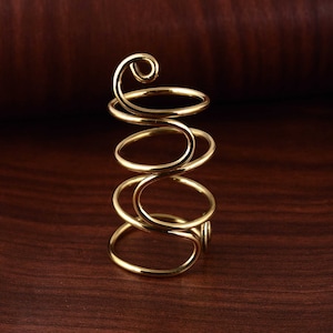 May include: A gold-coloured metal ring with a spiral design. The ring is made of multiple coils of wire that are twisted together.