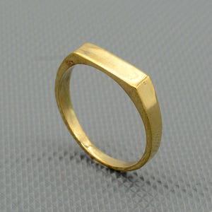 May include: A gold-colored band ring with a flat, rectangular top.