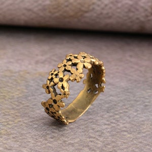 Może przedstawiać: Złoty pierścionek z delikatnym wzorem kwiatowym. Pierścionek wykonany jest z szeregu małych, połączonych ze sobą kwiatów.