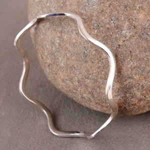 May include: A silver wavy bangle bracelet. The bracelet is made of a thin, smooth metal and has a simple, elegant design.