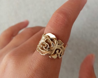 Può includere: Un anello d'oro con un designo di rosa dettagliato. La rosa è l'elemento principale dell'anello, con dettagli intricati nei petali e nelle foglie.