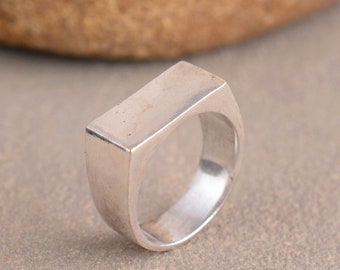 May include: A silver ring with a rectangular top. The ring is made of a smooth metal and has a simple design.
