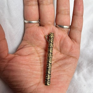 May include: A gold-colored metal pendant with intricate floral designs. The pendant has a loop at the top for attaching to a chain or cord.