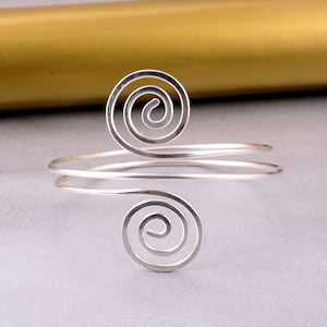 May include: Silver bracelet with two spiral designs. The bracelet is made of thin wire and is open on one side.