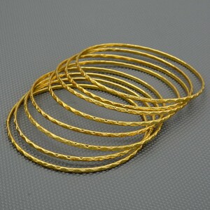 May include: A set of eight gold-toned bangles with a textured diamond pattern. The bangles are stacked on top of each other.