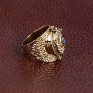 Puede incluir: Un anillo de oro con un compartimento con bisagras y una piedra preciosa azul. El anillo est&aacute; decorado con intrincados dise&ntilde;os florales.
