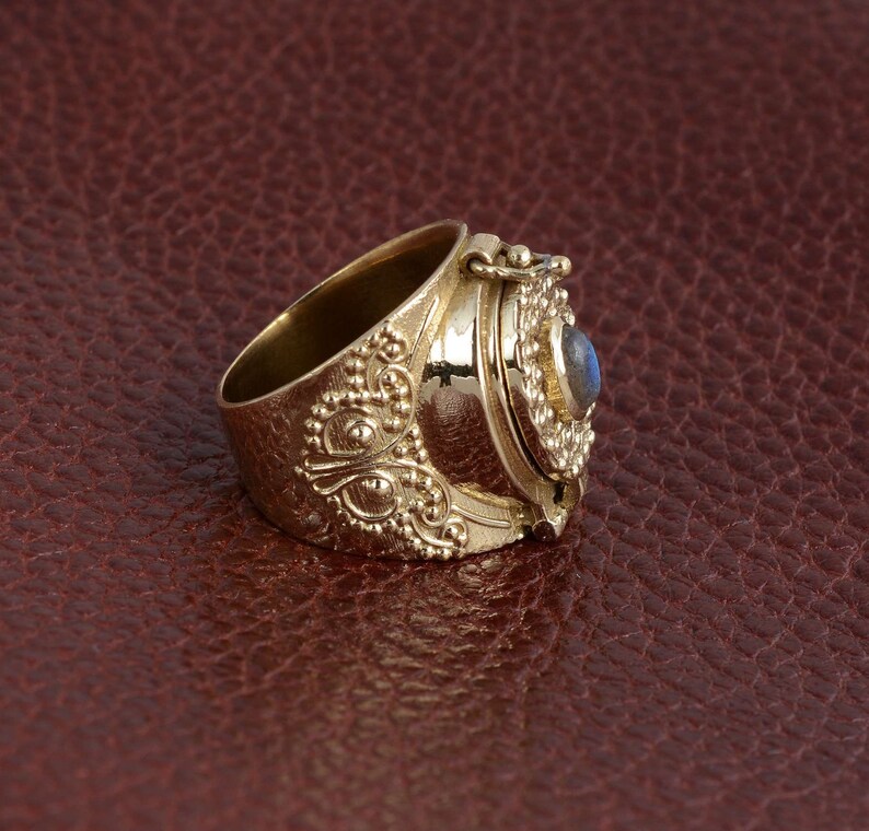 Puede incluir: Un anillo de oro con un compartimento con bisagras y una piedra preciosa azul. El anillo est&aacute; decorado con intrincados dise&ntilde;os florales.