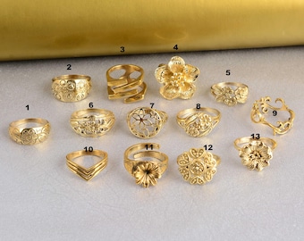 May include: A set of 13 gold-toned rings with various floral and geometric designs. The rings are arranged in a row on a gold surface.