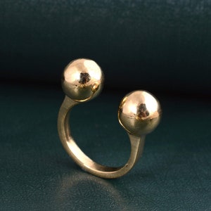 May include: A gold-toned ring with two round, smooth spheres on either side of the band.