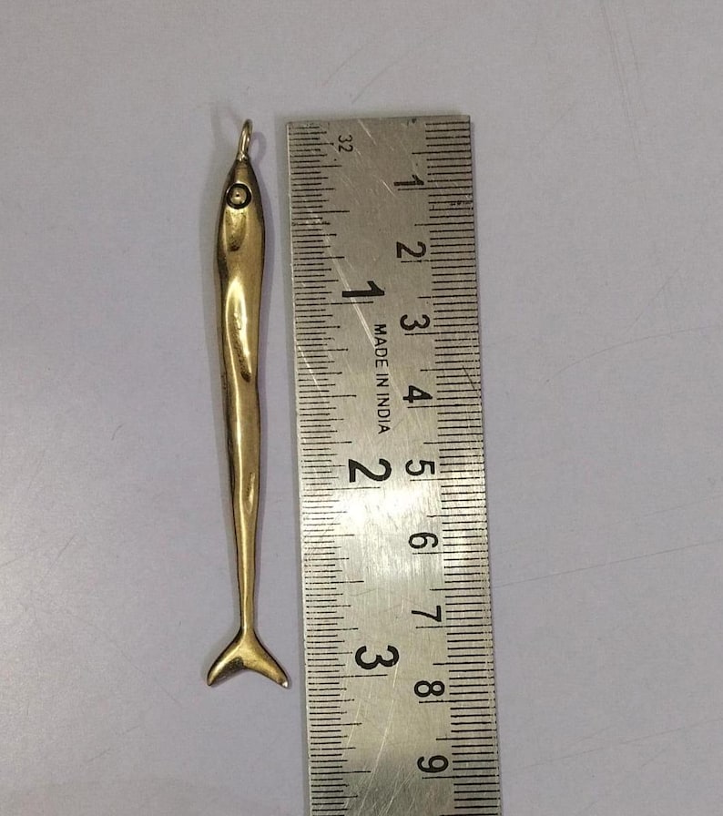 Op de afbeelding: Een gouden vis-hanger, ongeveer 5 cm lang, met een lus aan de bovenkant om aan een ketting of armband te bevestigen. De hanger is gedetailleerd met een getextureerd oppervlak en een gevorkte staart.