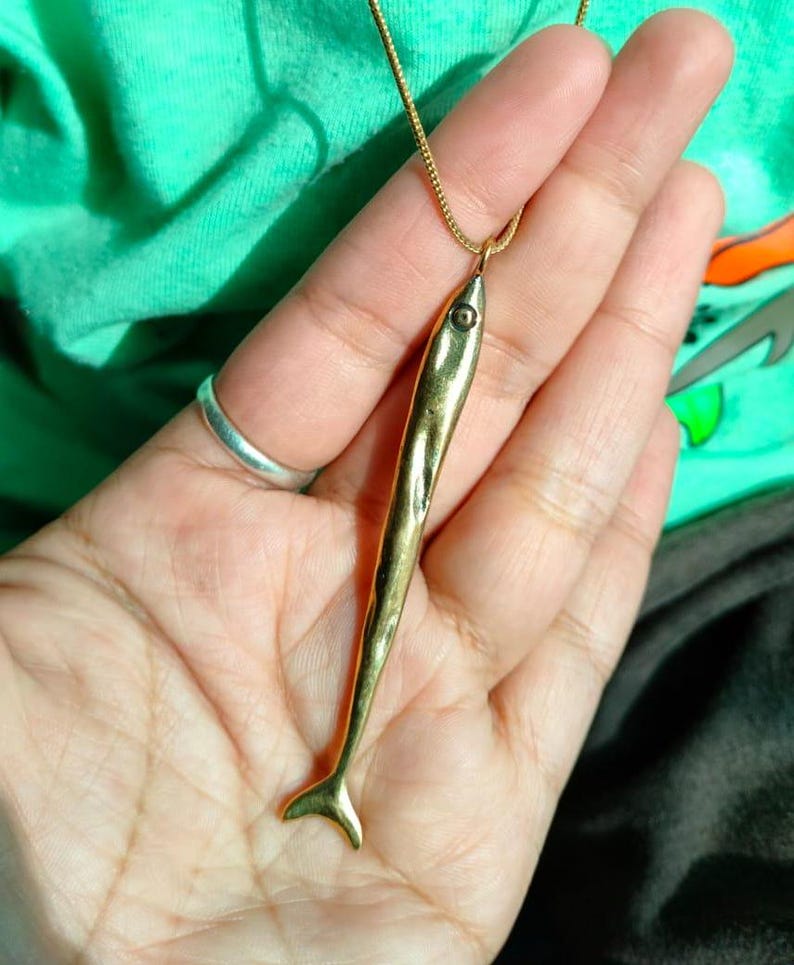 Op de afbeelding: Een gouden vis-hangerketting met een gedetailleerd ontwerp. De hanger hangt aan een gouden ketting.