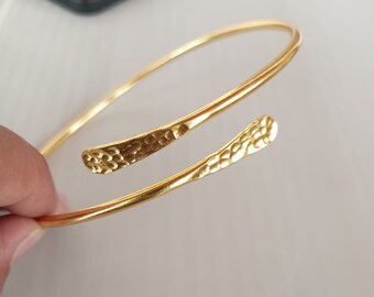 May include: A gold-toned bangle bracelet with a hammered texture. The bracelet is open and has a simple design.