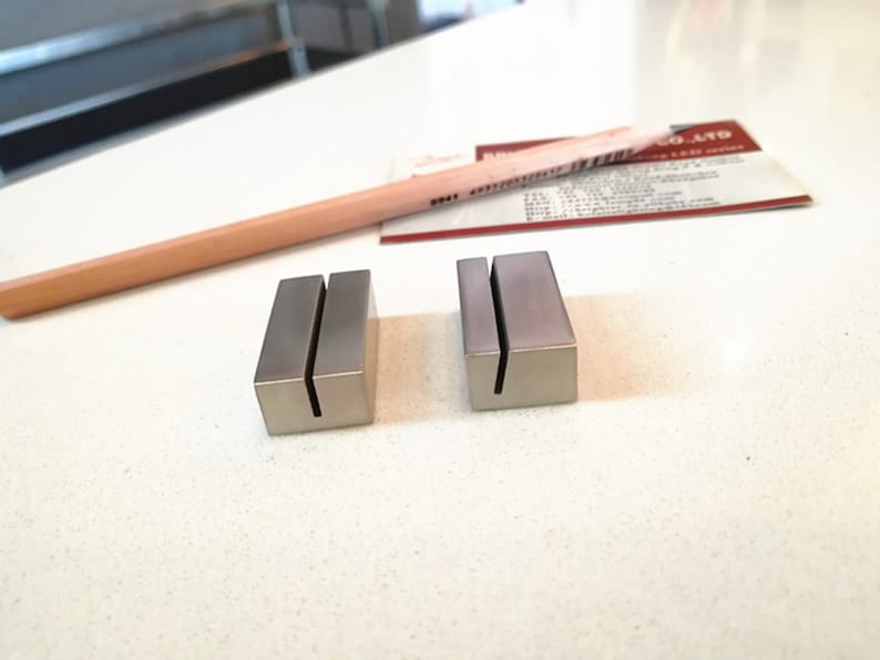 May include: Two silver metal business card holders with a slot for cards. The holders are on a white surface.