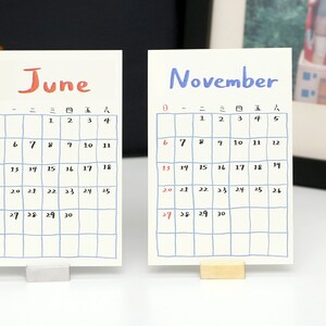 May include: Two white calendar cards with blue grid lines and handwritten numbers. The top card says "June" in red and the bottom card says "November" in blue.