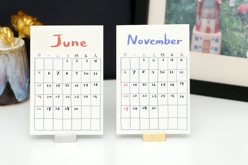 May include: Two white calendar cards with blue grid lines and handwritten numbers. The top card says "June" in red and the bottom card says "November" in blue.
