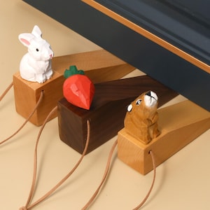 Pode incluir: Três batentes de porta de madeira com figuras esculpidas de animais e vegetais. Um batente de madeira clara tem um coelho branco, um de madeira escura tem uma cenoura vermelha e um de madeira clara tem um esquilo castanho. Incluem um cordão de couro.