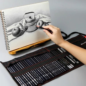 May include: A black canvas roll-up case with a red zipper and a set of 72 graphite pencils. The case is open and the pencils are arranged in rows. The pencils are all different shades of gray.