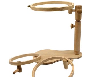 May include: A wooden embroidery hoop stand with three hoops of different sizes. The stand has a wooden base and a rotating arm that holds the hoop.