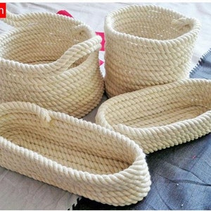 May include: Four natural-colored rope baskets, two oval and two round, with one round basket featuring a handle. The baskets are made of thick, woven rope and are perfect for storage or display.