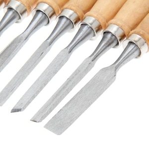 Puede incluir: Conjunto de seis cinceles para tallar madera con mangos de madera y hojas de metal. Los cinceles est&aacute;n dispuestos en una fila, con las hojas mirando hacia el espectador.