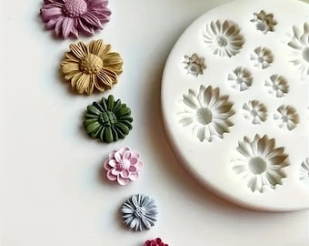 May include: A collection of colorful, daisy-shaped resin embellishments in shades of purple, gold, green, pink, gray, and red. A white silicone mold with daisy impressions is also present, suggesting a crafting theme.
