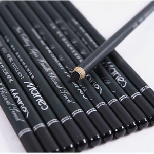 Pu&ograve; includere: Un set di matite di carbone nero con lettere argentate che recitano "Marie's Calling Taper Handle Charcoal Pencil" e "EXTRA SOFT".