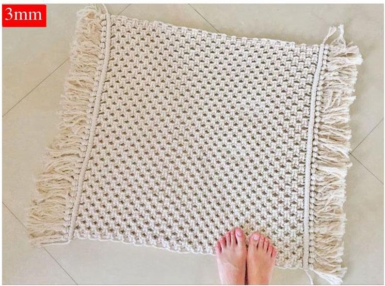 May include: A white macrame rug with fringe on all sides. The rug is made with a simple knot pattern and has a natural, bohemian style.