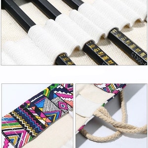 May include: A white canvas pencil case with a geometric pattern on the front and a rope handle. The case has multiple slots for pencils and is lined with white fabric. The case is empty and the pencils are not included.