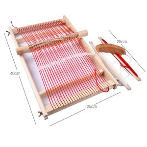 Pode incluir: Um tear de madeira com fio vermelho e um pente branco. O tear mede 25 cm por 40 cm.