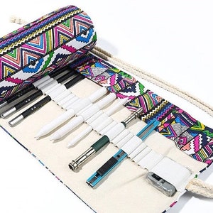 May include: A white canvas roll-up pencil case with a colorful geometric pattern. The case is open and has a variety of pencils, pens, and a utility knife inside.