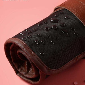 May include: A rolled-up black and brown canvas pouch with a brown leather strap. The pouch is waterproof and has water droplets on the surface. The text "Waterproof material" and "Durable wear" is visible above the pouch.